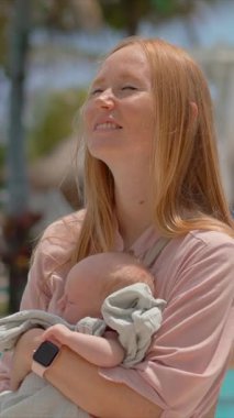 Bir anne ve yeni doğan bebeği, tropik bir sahil beldesinde güneşli bir günün tadını çıkarıyorlar. Tropiklerin sıcaklığı ve güzelliği ile çevrili huzurlu bir bağ, rahatlama ve aile zamanı..