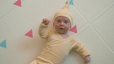 Sarı kıyafetli, şapkalı, yumuşak halıda yatan sevimli yeni doğmuş bebek. Samimi, sıcak ve çocukluk dönemi konsepti. Yavaş çekim videosu