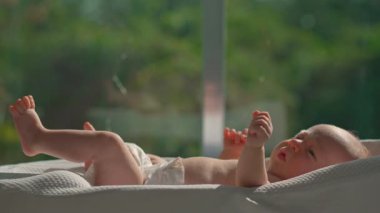 Yeni doğmuş bir bebek, güneş ışığının açık olduğu bir pencerenin yakınındaki bebek kozasında dinlenir ve sağlıklı dozda D vitamini için doğal güneş ışığını emer. Yeni doğanlar için güneşlenmenin önemini vurgulayan huzurlu bir an.