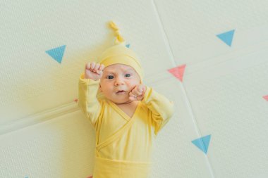 Sarı şapkalı sevimli bebek oyun hasırının üzerinde yatıyor. Yumuşak dokuları ve parlak renkleriyle yeni doğmuş gibi. Bebek gelişimi, duyusal oyun ve erken çocukluk kavramı..