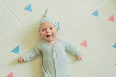 Yeşil şapkalı sevimli bebek oyun hasırının üzerinde yatıyor. Yumuşak dokuları ve parlak renkleriyle yeni doğmuş gibi. Bebek gelişimi, duyusal oyun ve erken çocukluk kavramı..