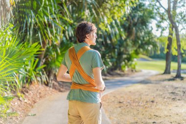 Babam küçük bebeğini parkta sarı bir askıda tutuyor. Sıcak ve sevgi dolu bir aile anı. Bebek giyimi, babalık ve ebeveyn-çocuk bağlama kavramı..
