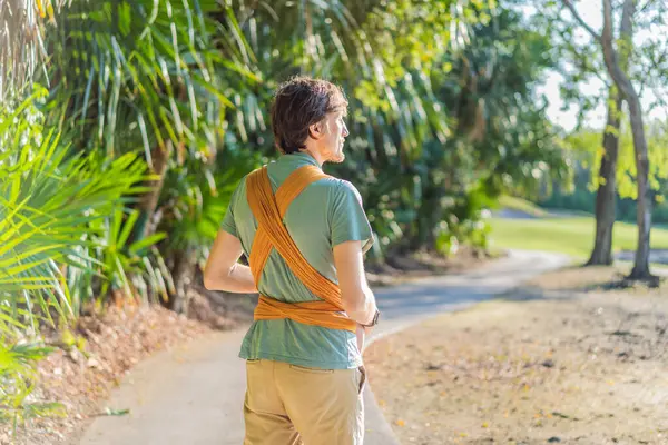 Babam küçük bebeğini parkta sarı bir askıda tutuyor. Sıcak ve sevgi dolu bir aile anı. Bebek giyimi, babalık ve ebeveyn-çocuk bağlama kavramı..