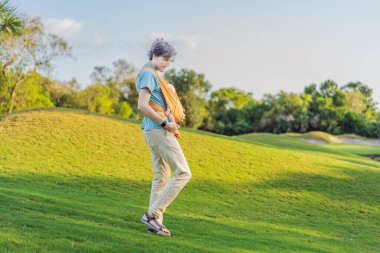 Babam küçük bebeğini parkta sarı bir askıda tutuyor. Sıcak ve sevgi dolu bir aile anı. Bebek giyimi, babalık ve ebeveyn-çocuk bağlama kavramı..