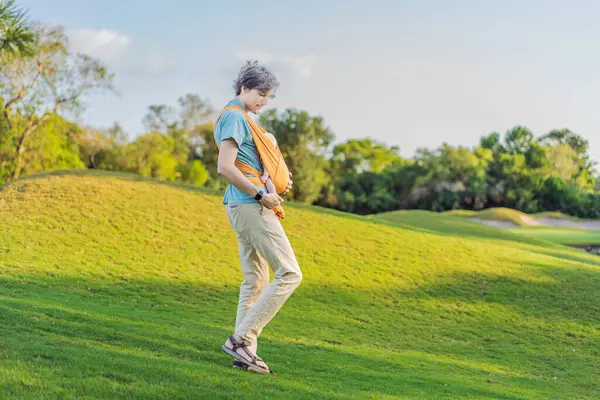 Babam küçük bebeğini parkta sarı bir askıda tutuyor. Sıcak ve sevgi dolu bir aile anı. Bebek giyimi, babalık ve ebeveyn-çocuk bağlama kavramı..