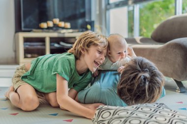 Baba, oğul ve yeni doğan bebek sıcak bir kreşte yerde yatıyorlar ve yeni aile üyelerinin gelişini kutluyorlar. Ebeveynlik, bağlılık ve aile sevgisi kavramı.
