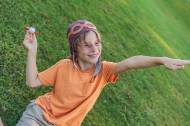 Pilot şapkası takan bir çocuk oyuncak bir uçakla çimlerde koşuyor, maceralar hayal ediyor. Çocukluk, hayal gücü ve özgürlük kavramı..