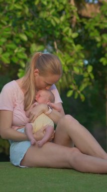 Genç bir kadın yemyeşil bir çimenlikte gülerek oturuyor, yeni doğmuş bebeğini elinde tutuyor. Doğayla çevrili neşeli ve hassas bir bağ, aşk ve mutluluk anı.