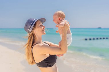 Anne yeni doğmuş bebeğini turkuaz denizde kucaklıyor, huzurlu ve sevgi dolu bir anı paylaşıyor. Aile bağı, annelik ve bebek konseptiyle seyahat..