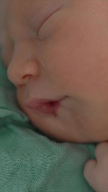 Uyuyan yeni doğmuş bir bebeğin yumuşak bir muslin battaniyeye sarılı olduğu yakın çekim videosu. Yumuşak ve huzurlu bir an, yeni doğmuş bir bebeğin masumiyetini ve huzurunu yakalıyor.