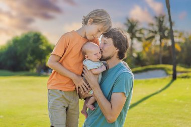 Baba, büyük oğul ve parkta bir çayırda yeni doğmuş bebek. Aile, doğada birlikte kaliteli zaman geçirir. Ebeveynlik, sevgi ve aile bağı kavramı.