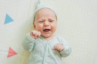 Yeşil şapkalı sevimli bebek oyun hasırının üzerinde yatıyor. Yumuşak dokuları ve parlak renkleriyle yeni doğmuş gibi. Bebek gelişimi, duyusal oyun ve erken çocukluk kavramı..