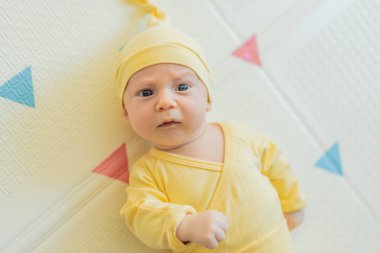 Sarı şapkalı sevimli bebek oyun hasırının üzerinde yatıyor. Yumuşak dokuları ve parlak renkleriyle yeni doğmuş gibi. Bebek gelişimi, duyusal oyun ve erken çocukluk kavramı..
