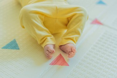 Sarı şapkalı sevimli bebek oyun hasırının üzerinde yatıyor. Yumuşak dokuları ve parlak renkleriyle yeni doğmuş gibi. Bebek gelişimi, duyusal oyun ve erken çocukluk kavramı..
