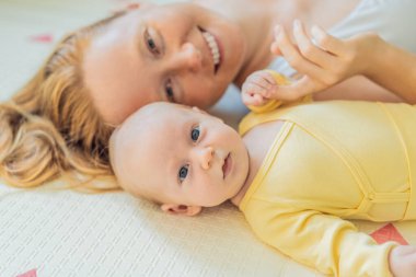 Anne ve bebek oyun hasırının üzerinde yatıyor. Hassas bağ anı, rahat çocukluk atmosferi ve erken gelişim. Ebeveynlik, sevgi ve bebek bakımı konsepti.