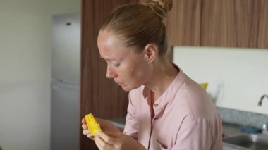 Genç bir kadın mutfakta duruyor, taze mangonun tadını çıkarıyor. Sağlıklı beslenmenin, tropikal lezzetlerin ve sıcak bir yuva ortamında ihtiyatlı yaşamanın basit ve canlı bir anı.