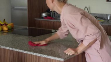 Genç bir kadın mutfak masasını temizliyor, evinde temizlik ve düzen sağlıyor. Basit ama önemli bir ev yapımı, bakım ve düzenli ve davetkar bir yer yaratma anı