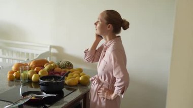 Mutfakta yemek pişirirken cep telefonuyla konuşan bir kadın. Meşgul ama rahat bir ev ortamında iletişim ve yemek hazırlama için uygun bir an.