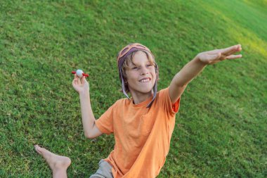 Pilot şapkası takan bir çocuk oyuncak bir uçakla çimlerde koşuyor, maceralar hayal ediyor. Çocukluk, hayal gücü ve özgürlük kavramı..