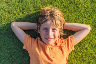 Yeşil çimenlerin üzerinde uzanmış kameraya bakan bir çocuk. Uzayı metin için kopyala. Çocukluk, ebeveynlik, eğitim ve çocuk gelişimi soruları.