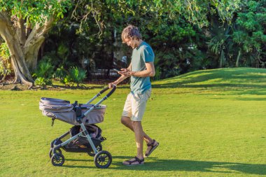 Babam telefonuna bakarken çimenli bir arazide bebek arabasını itiyor. Modern ebeveynlik kavramı, çoklu görev, günlük hayatta teknoloji ve iş-yaşam dengesi.