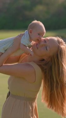 Genç bir kadın yemyeşil bir çimenlikte duruyor, yeni doğmuş bebeğini ellerinde tutuyor. Doğayla çevrili neşeli ve hassas bir bağ, aşk ve mutluluk anı.