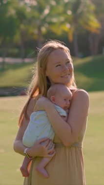 Genç bir kadın yemyeşil bir çimenlikte duruyor, yeni doğmuş bebeğini ellerinde tutuyor. Doğayla çevrili neşeli ve hassas bir bağ, aşk ve mutluluk anı.