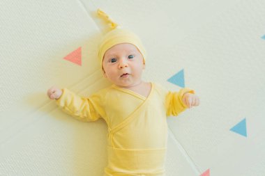 Sarı şapkalı sevimli bebek oyun hasırının üzerinde yatıyor. Yumuşak dokuları ve parlak renkleriyle yeni doğmuş gibi. Bebek gelişimi, duyusal oyun ve erken çocukluk kavramı..