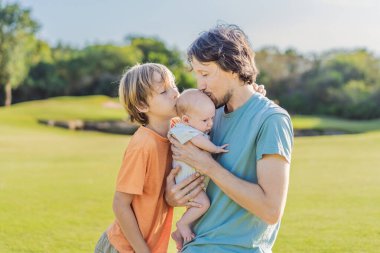 Baba, büyük oğul ve parkta bir çayırda yeni doğmuş bebek. Aile, doğada birlikte kaliteli zaman geçirir. Ebeveynlik, sevgi ve aile bağı kavramı.