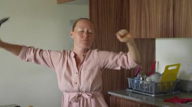 Genç bir kadın mutfakta yemek pişirirken neşeyle dans ediyor ve şarkı söylüyor. Sıcak bir ev ortamında yemek hazırlarken yaratıcılığın, kendini ifade etmenin ve keyif almanın neşeli ve neşeli bir anı.