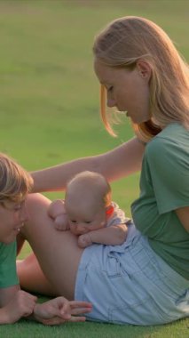 Genç bir anne, yemyeşil bir çimenlikte büyük oğlu ve yeni doğmuş çocuğuyla güneşli bir günün tadını çıkarır. Sevgi, bağ ve açık hava eğlencesiyle dolu neşeli bir aile anı ebeveynliği ve çocukluğu kutluyor.