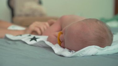 Emziği olan çıplak bir bebek su geçirmez bir peçetenin üzerine uzanır. Bezsiz geçen zamanın tadını çıkarır ve derileri nefes alır. Bebek bakımının gerekliliklerini vurgulayan huzurlu bir an, bebeğin tanıtımı için ideal.