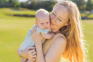 Anne ve yeni doğmuş bebek parkta bir çayırda. Doğadaki hassas bağ anı. Ebeveynlik, sevgi ve aile bağları kavramı.