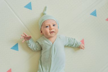 Yeşil şapkalı sevimli bebek oyun hasırının üzerinde yatıyor. Yumuşak dokuları ve parlak renkleriyle yeni doğmuş gibi. Bebek gelişimi, duyusal oyun ve erken çocukluk kavramı..