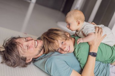 Baba, oğul ve yeni doğan bebek sıcak bir kreşte yerde yatıyorlar ve yeni aile üyelerinin gelişini kutluyorlar. Ebeveynlik, bağlılık ve aile sevgisi kavramı.