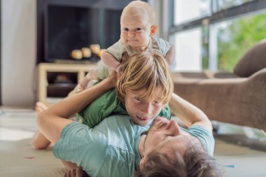 Baba, oğul ve yeni doğan bebek sıcak bir kreşte yerde yatıyorlar ve yeni aile üyelerinin gelişini kutluyorlar. Ebeveynlik, bağlılık ve aile sevgisi kavramı.