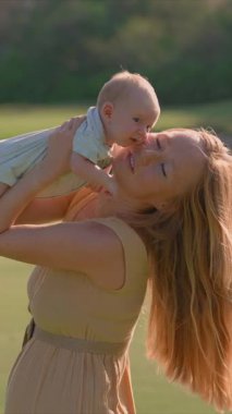 Genç bir kadın yemyeşil bir çimenlikte duruyor, yeni doğmuş bebeğini ellerinde tutuyor. Doğayla çevrili neşeli ve hassas bir bağ, aşk ve mutluluk anı.