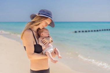 Anne yeni doğmuş bebeğini turkuaz denizde kucaklıyor, huzurlu ve sevgi dolu bir anı paylaşıyor. Aile bağı, annelik ve bebek konseptiyle seyahat..