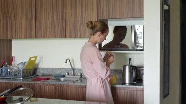 Genç bir kadın mutfakta bir fincan çay hazırlıyor ve onu içmekten zevk alıyor. Sıcak ve davetkar bir yuva ortamında rahatlatıcı bir öz bakım, rahatlama ve farkındalık anı.