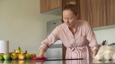 Genç bir kadın mutfak masasını temizliyor, evinde temizlik ve düzen sağlıyor. Basit ama önemli bir ev yapımı, bakım ve düzenli ve davetkar bir yer yaratma anı