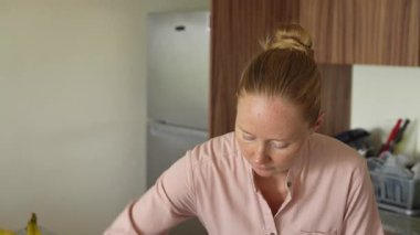 Genç bir kadın mutfak masasını temizliyor, evinde temizlik ve düzen sağlıyor. Basit ama önemli bir ev yapımı, bakım ve düzenli ve davetkar bir yer yaratma anı