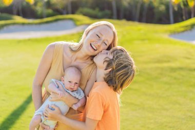 Anne, büyük oğul ve parkta bir çayırda yeni doğmuş bebek. Aile, doğada birlikte kaliteli zaman geçirir. Ebeveynlik, sevgi ve aile bağı kavramı.