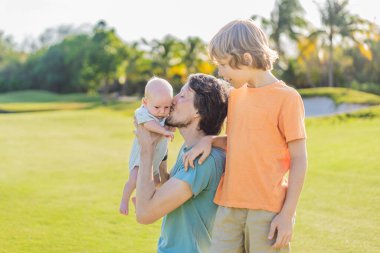 Baba, büyük oğul ve parkta bir çayırda yeni doğmuş bebek. Aile, doğada birlikte kaliteli zaman geçirir. Ebeveynlik, sevgi ve aile bağı kavramı.