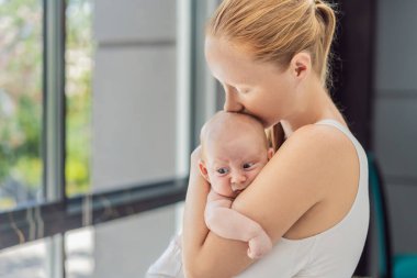 Anne evde bebeğine nazikçe sarılıyor, sıcak ve sevgi dolu bir anı paylaşıyor. Ebeveynlik, aile bağı ve anne sevgisi kavramı..