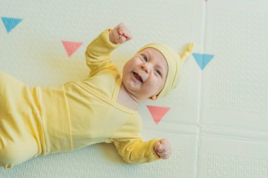 Sarı şapkalı sevimli bebek oyun hasırının üzerinde yatıyor. Yumuşak dokuları ve parlak renkleriyle yeni doğmuş gibi. Bebek gelişimi, duyusal oyun ve erken çocukluk kavramı..