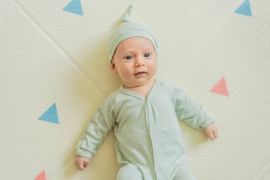 Yeşil şapkalı sevimli bebek oyun hasırının üzerinde yatıyor. Yumuşak dokuları ve parlak renkleriyle yeni doğmuş gibi. Bebek gelişimi, duyusal oyun ve erken çocukluk kavramı..