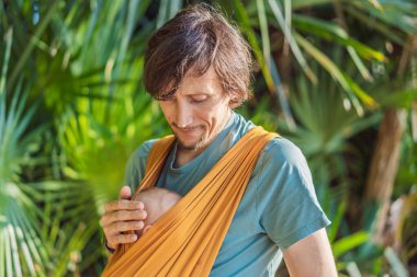 Babam küçük bebeğini parkta sarı bir askıda tutuyor. Sıcak ve sevgi dolu bir aile anı. Bebek giyimi, babalık ve ebeveyn-çocuk bağlama kavramı..