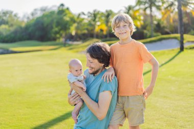 Baba, büyük oğul ve parkta bir çayırda yeni doğmuş bebek. Aile, doğada birlikte kaliteli zaman geçirir. Ebeveynlik, sevgi ve aile bağı kavramı.