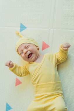 Sarı şapkalı sevimli bebek oyun hasırının üzerinde yatıyor. Yumuşak dokuları ve parlak renkleriyle yeni doğmuş gibi. Bebek gelişimi, duyusal oyun ve erken çocukluk kavramı..