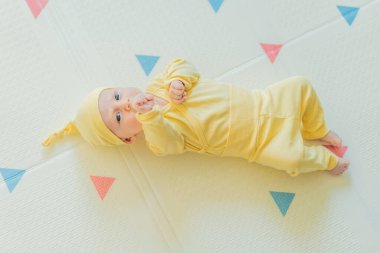 Sarı şapkalı sevimli bebek oyun hasırının üzerinde yatıyor. Yumuşak dokuları ve parlak renkleriyle yeni doğmuş gibi. Bebek gelişimi, duyusal oyun ve erken çocukluk kavramı..